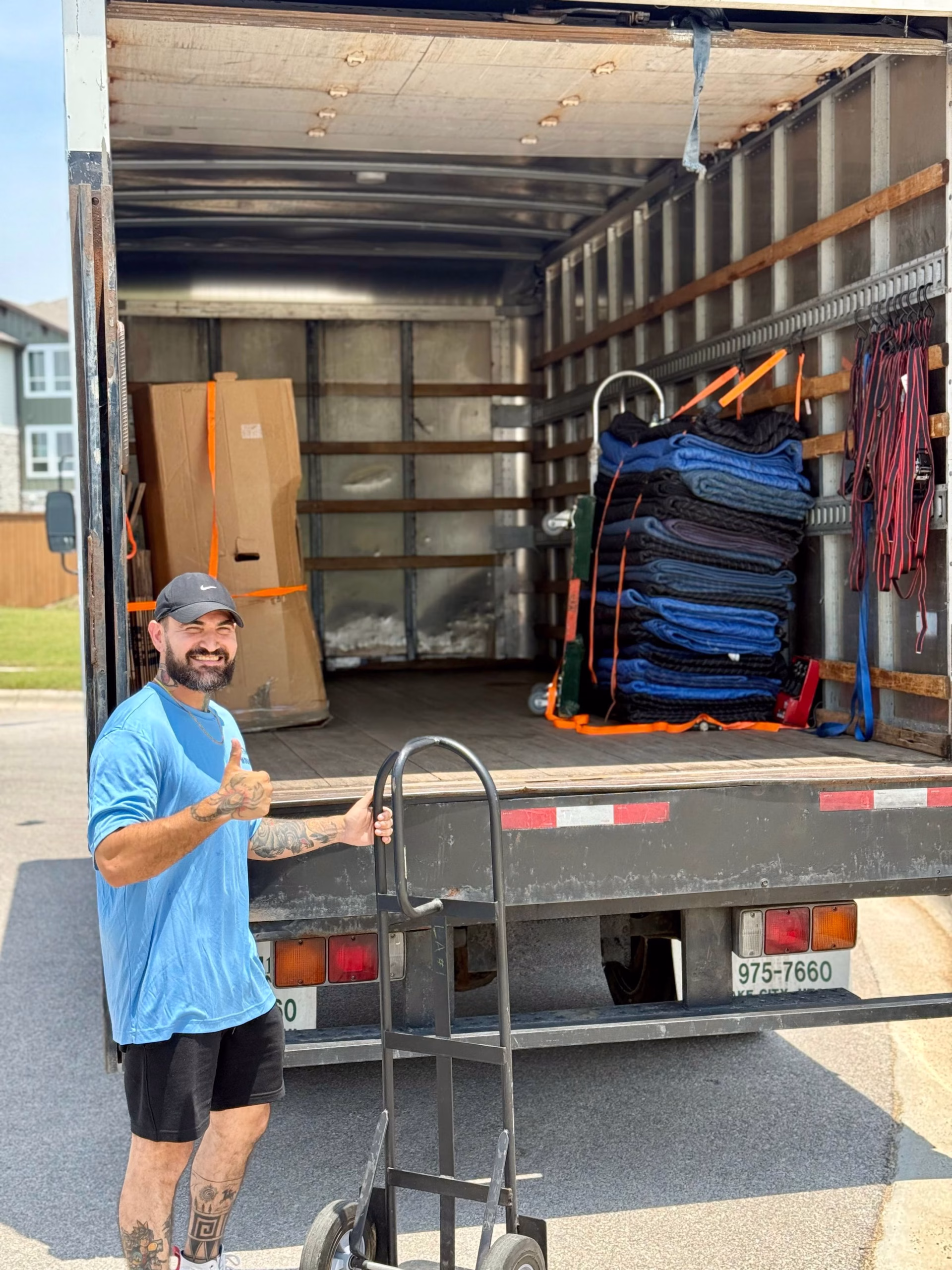 An Austin Moving Company professional giving a thumbs up next to a hand truck and moving van.