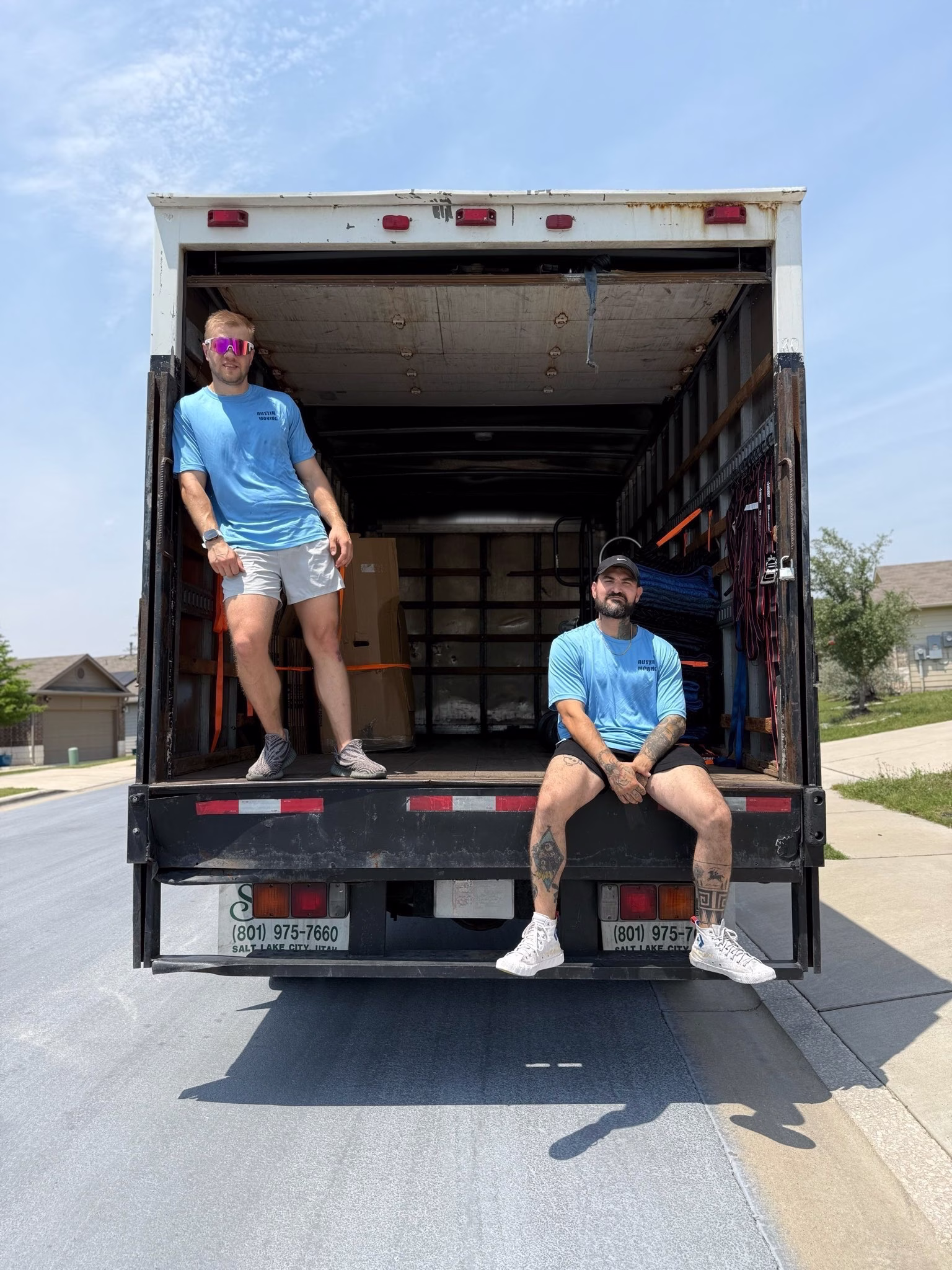 Two professional Austin movers posing confidently inside an open moving truck.