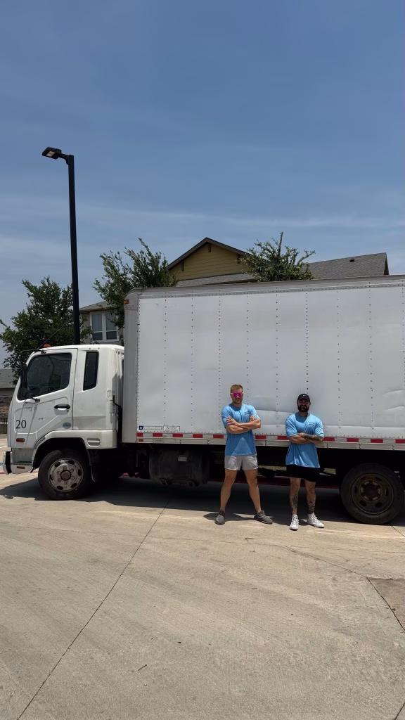 Two confident local movers standing with their arms crossed next to the side of a large white moving truck.