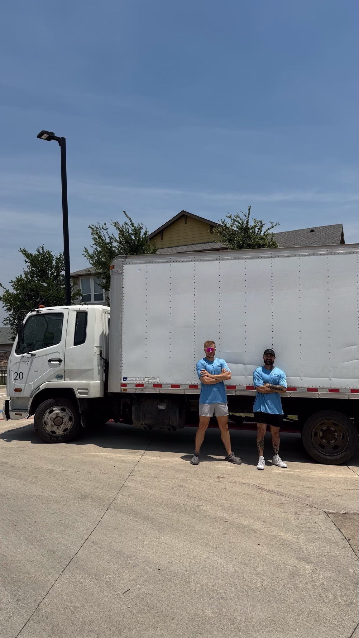 Two confident local movers standing with their arms crossed next to the side of a large white moving truck.
