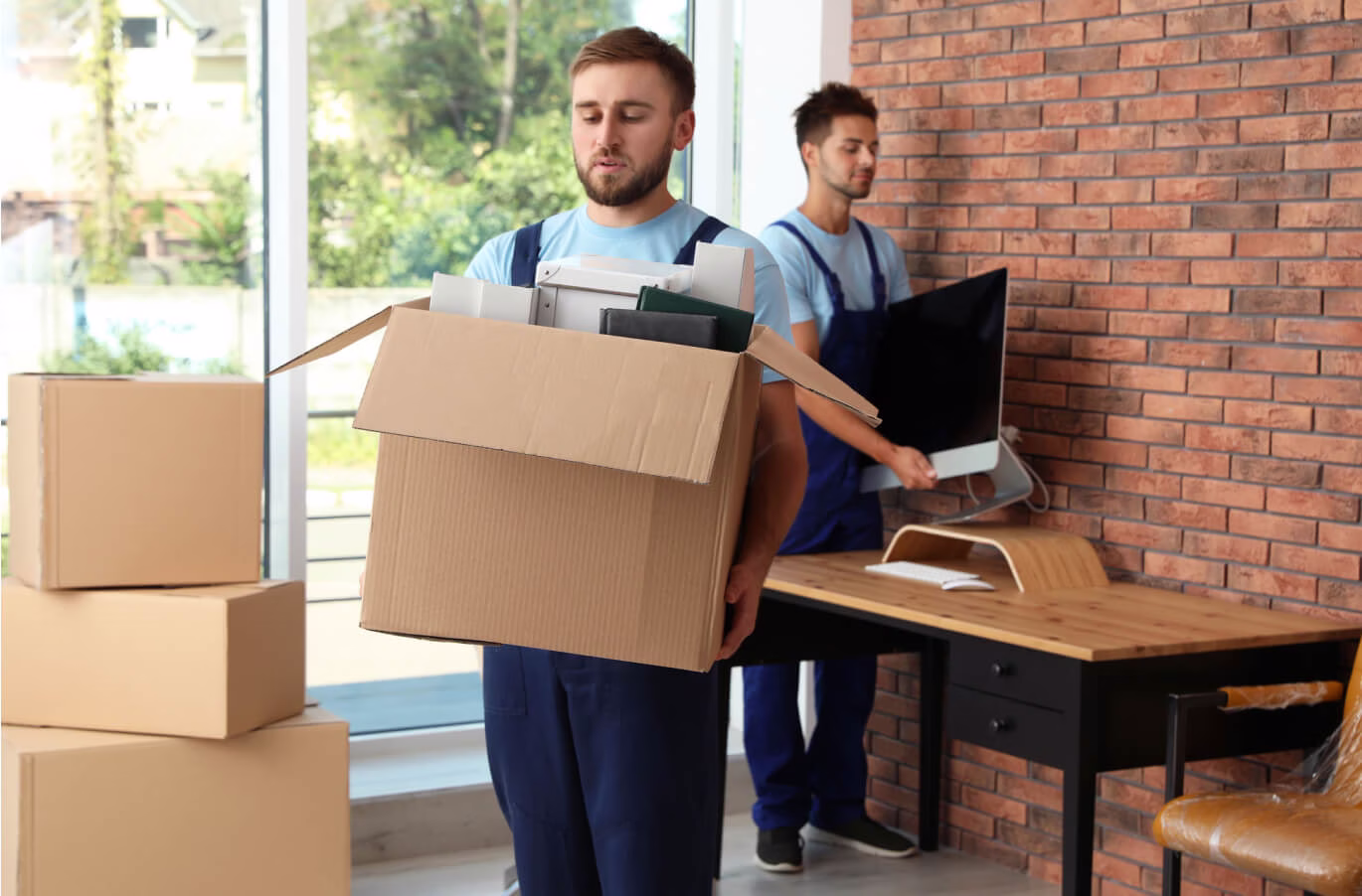 Professional movers carefully carrying heavy cardboard boxes and a computer monitor during a commercial office relocation.